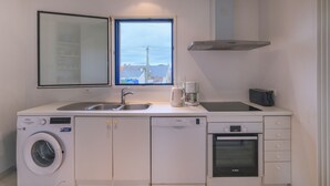 Cocina compacta con lavadora, lavavajillas, horno y ventana con vistas a edificios.