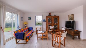 Una sala de estar con sofá, sillas, una mesa, televisor y estantería.