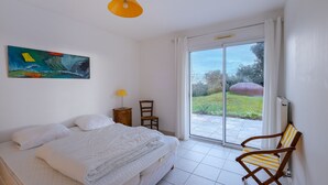 Un dormitorio con cama, una silla, un cuadro y vistas a través de un ventanal corredizo.