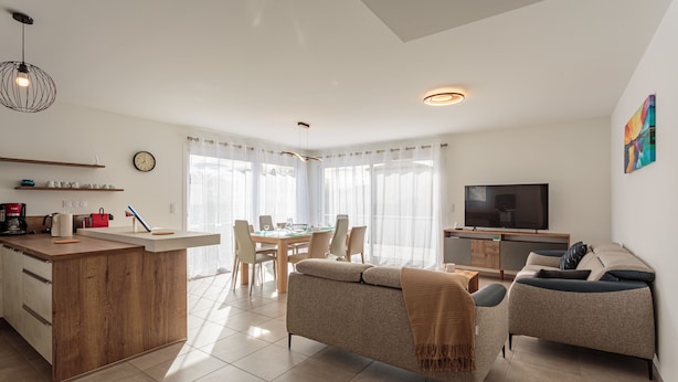 Un appartement moderne comprenant une cuisine, un coin repas et un salon. Il est équipé d’une télévision, d’un canapé et d’une table à manger avec des chaises.