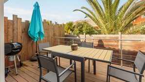 Eine Terrasse im Freien mit Holztisch und -stühlen, einem Grill und einem Holzzaun.