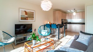 A modern living room with a sofa, TV, and a dining area with chairs and a table.
