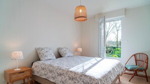 A bedroom with a bed, two bedside lamps, a window with a view, and a chair.