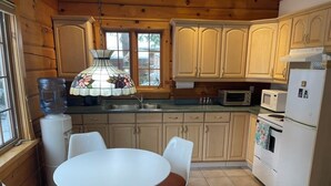 Une cuisine avec des meubles en bois, un plan de travail blanc, une table ronde avec des chaises, un distributeur d’eau et un four à micro-ondes.