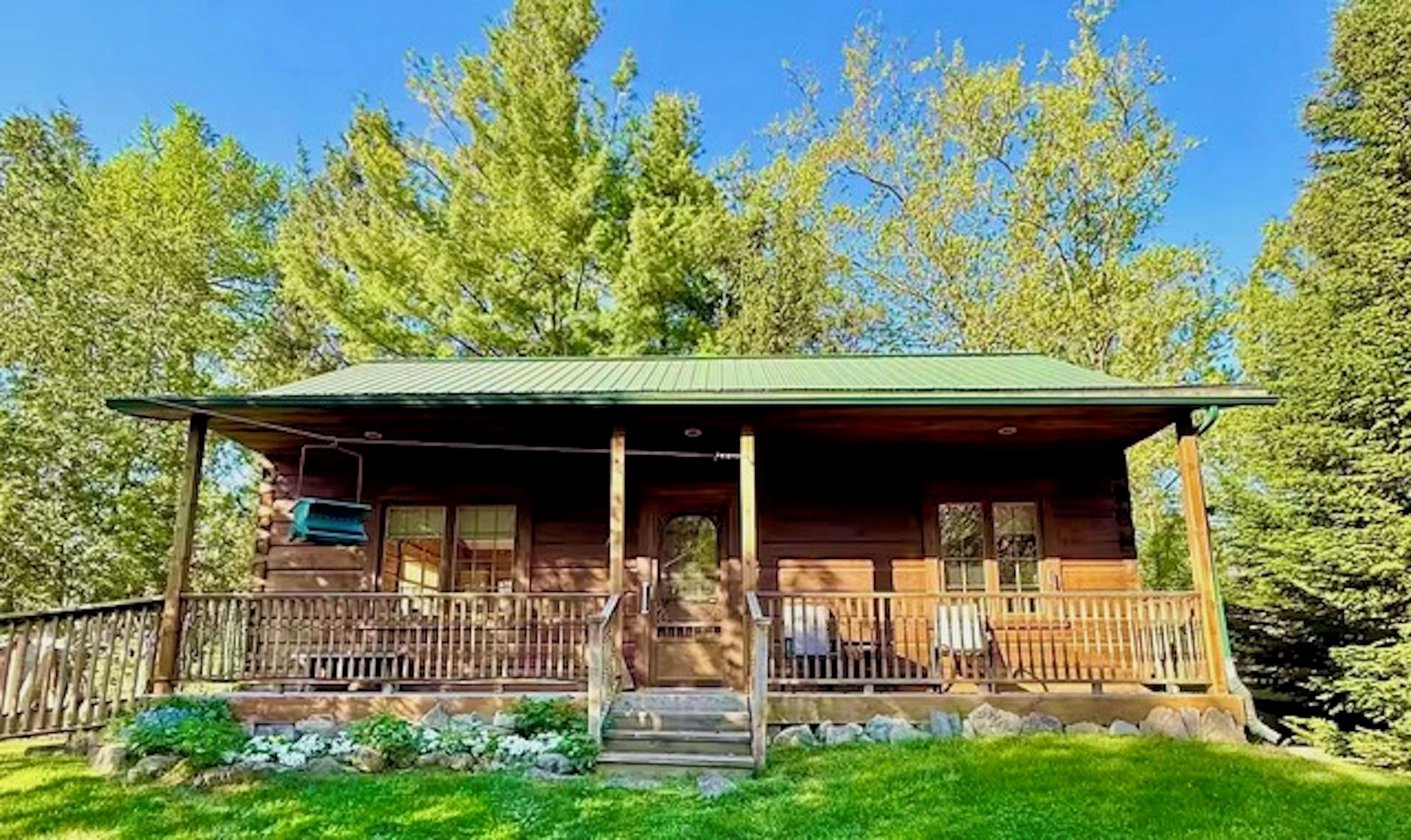 A wooden cabin with a porch, surrounded by trees.