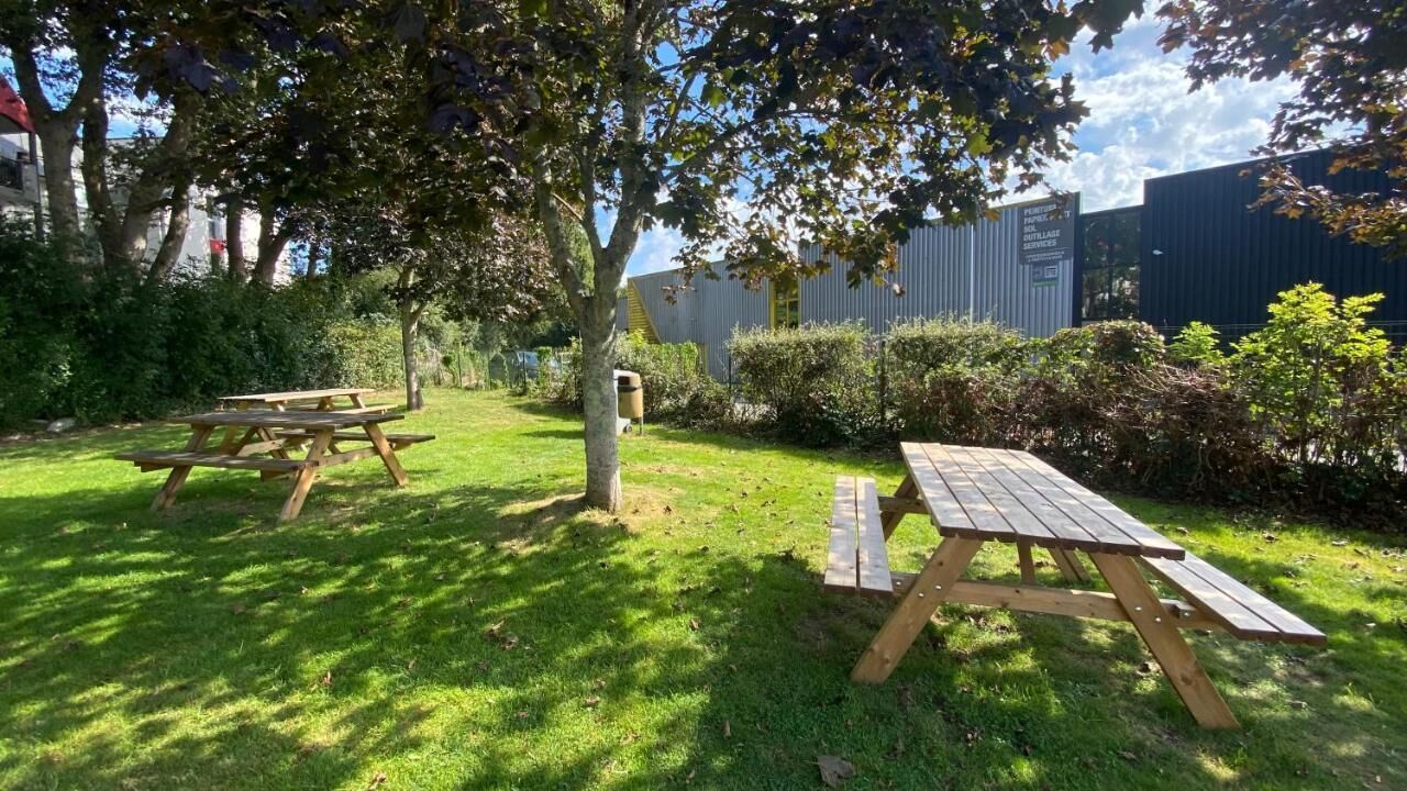 Un espacio al aire libre con césped, mesas de picnic y un edificio al fondo.
