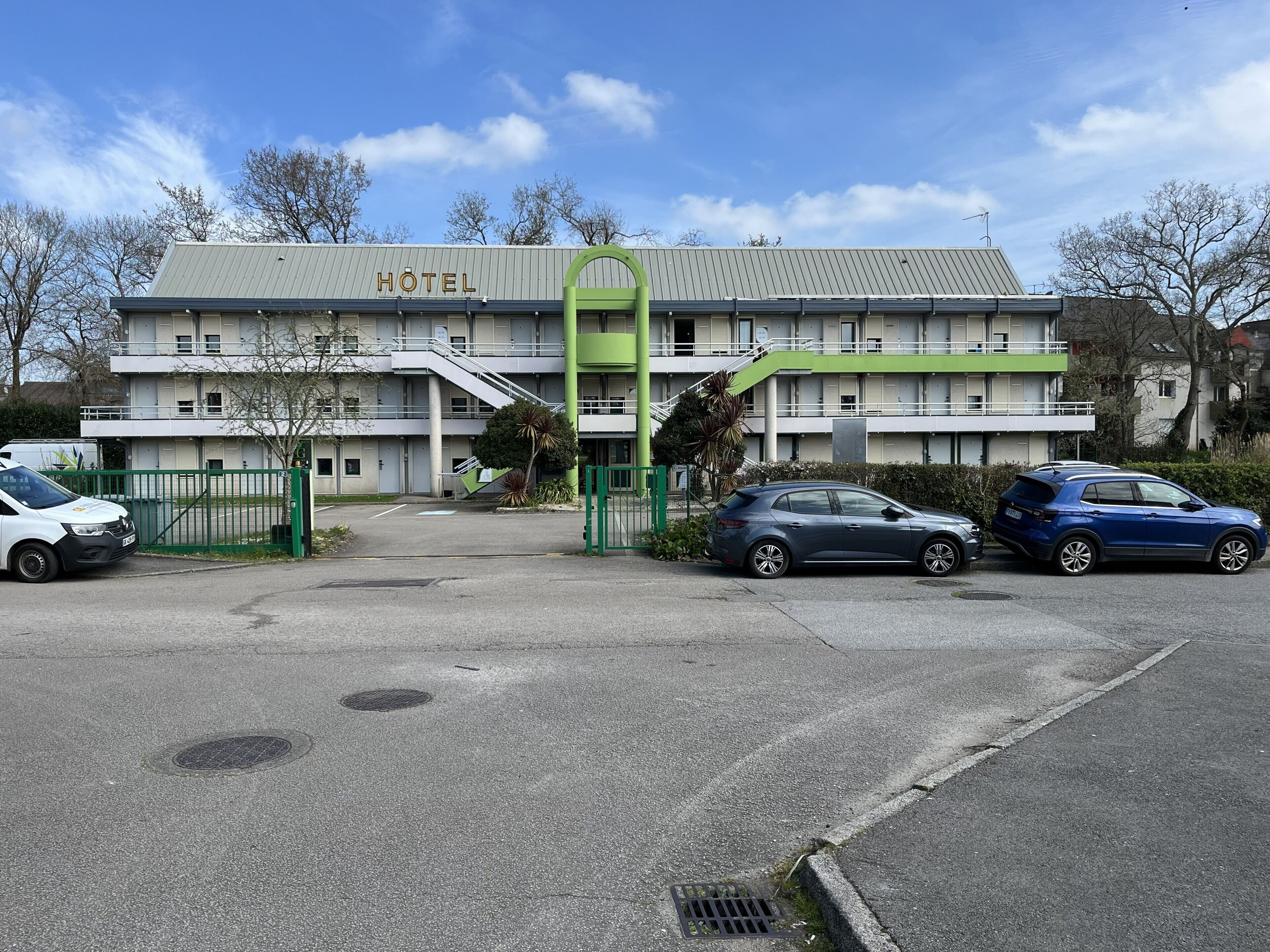 Ein Hotel mit Schilder, einem grünen Eingang und zwei geparkten Autos davor.