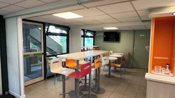 A room with a long table, multiple chairs, a television on the wall, and a door with a window.