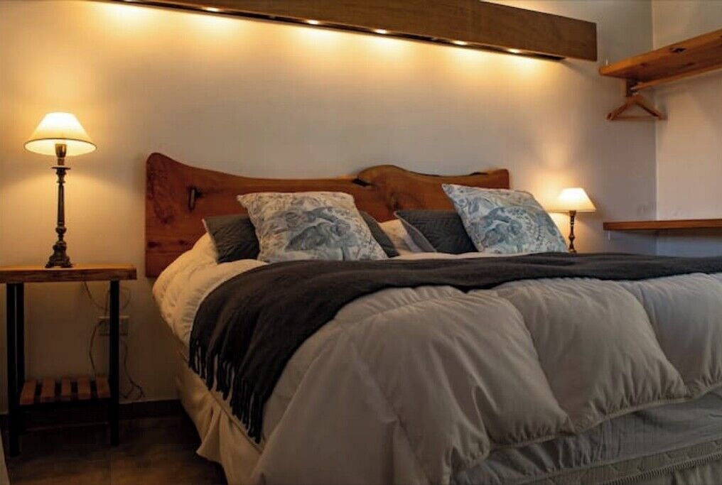 A bed with a wooden headboard, two bedside tables with lamps, and a hanging light fixture above the bed.