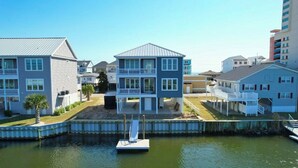 A waterfront property with two-story buildings, a dock, and a small boat. - Simply Blessed- 5BR/5.5BA Channel House-Pool (North Myrtle Beach)