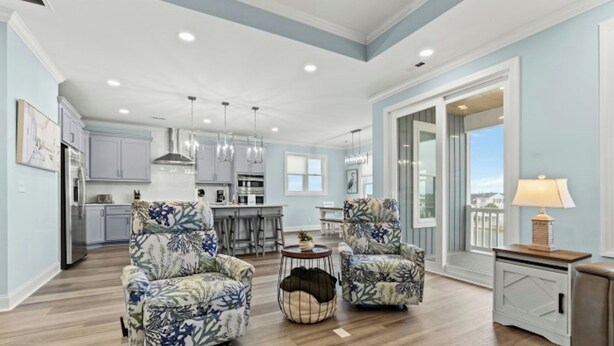 A spacious living room with two patterned armchairs, a coffee table, and a view of the kitchen and dining area. - Simply Blessed- 5BR/5.5BA Channel House-Pool (North Myrtle Beach)