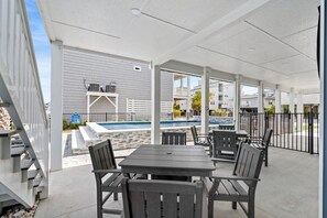 A covered outdoor area with a pool, seating, and a view of a building with a balcony.