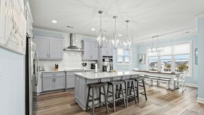 A modern kitchen with a large island, bar stools, and a view of the outside. - Simply Blessed- 5BR/5.5BA Channel House-Pool (North Myrtle Beach)