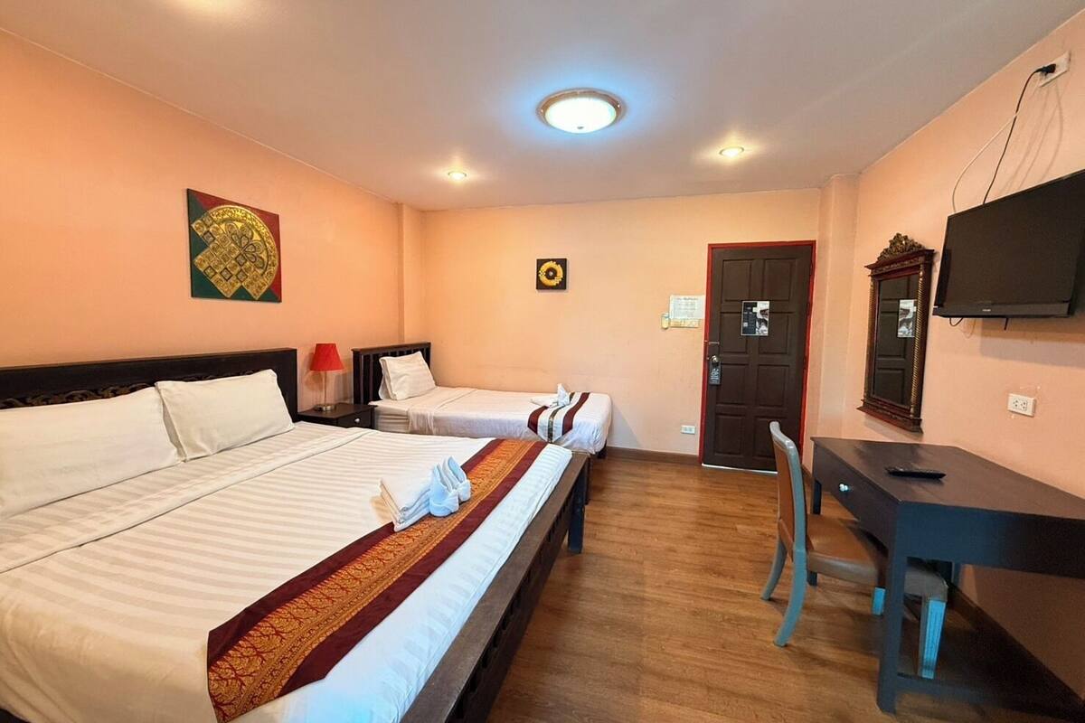 A hotel room with two beds, a desk, a chair, a television, and a door.
