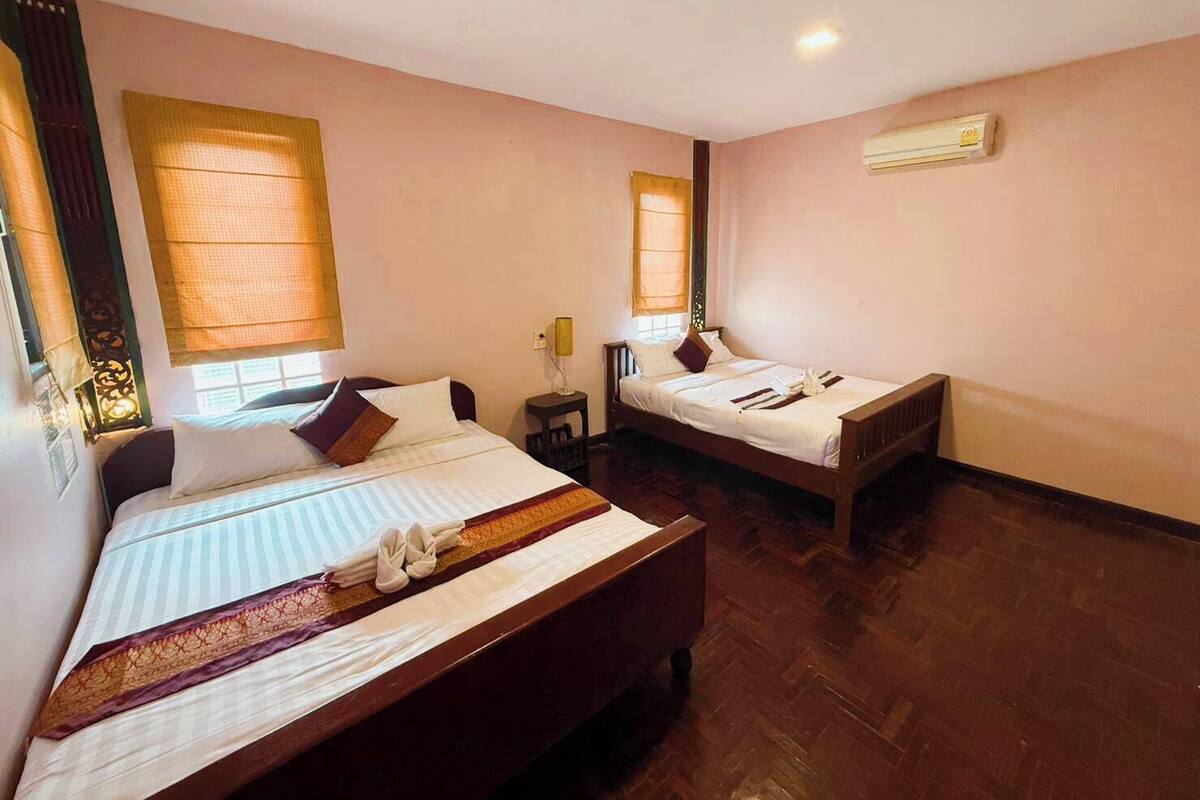 A hotel room with two beds, a wooden floor, and a window with a curtain.