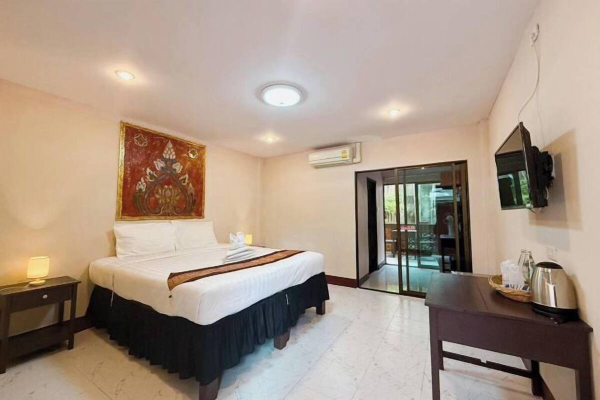 A hotel room with a bed, bedside table, artwork, air conditioning unit, and a view through a glass door.