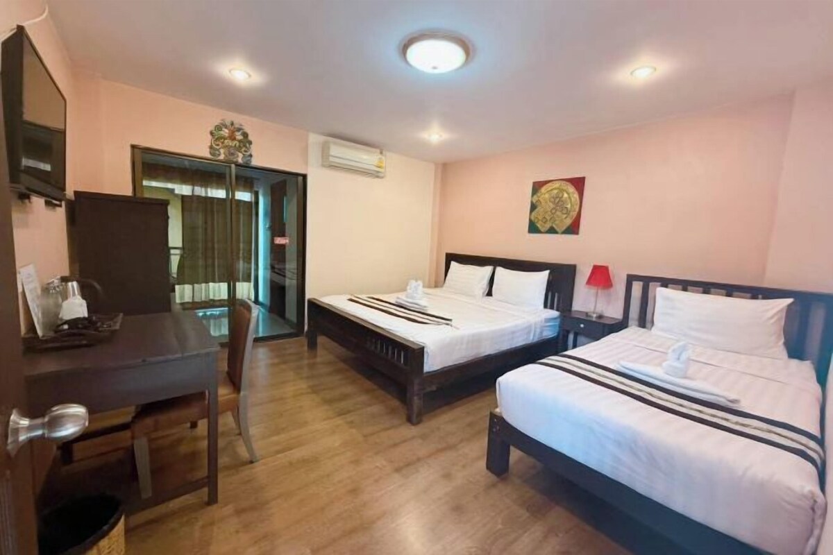 A hotel room with two beds, a desk, a chair, and a door leading to a balcony.