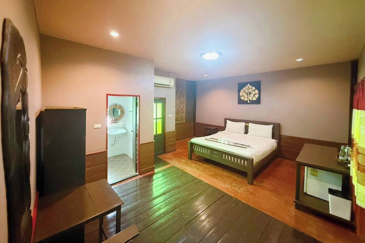 A hotel room with a bed, a desk, a chair, a mirror, and a door leading to a bathroom.