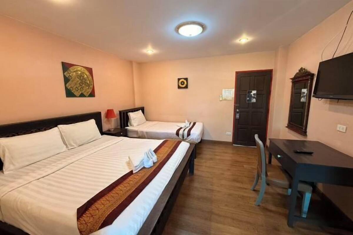 A hotel room with two beds, a desk, a TV, and a door.