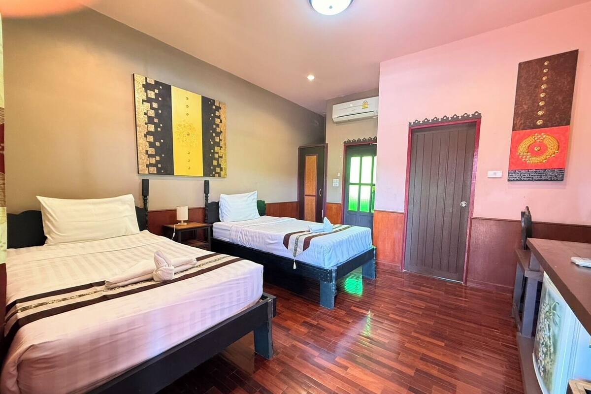 A hotel room with two beds, a wooden floor, a door, and a wall with artwork.