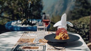 A table with a dessert, a glass of red wine, and a water glass, set against a mountainous backdrop.