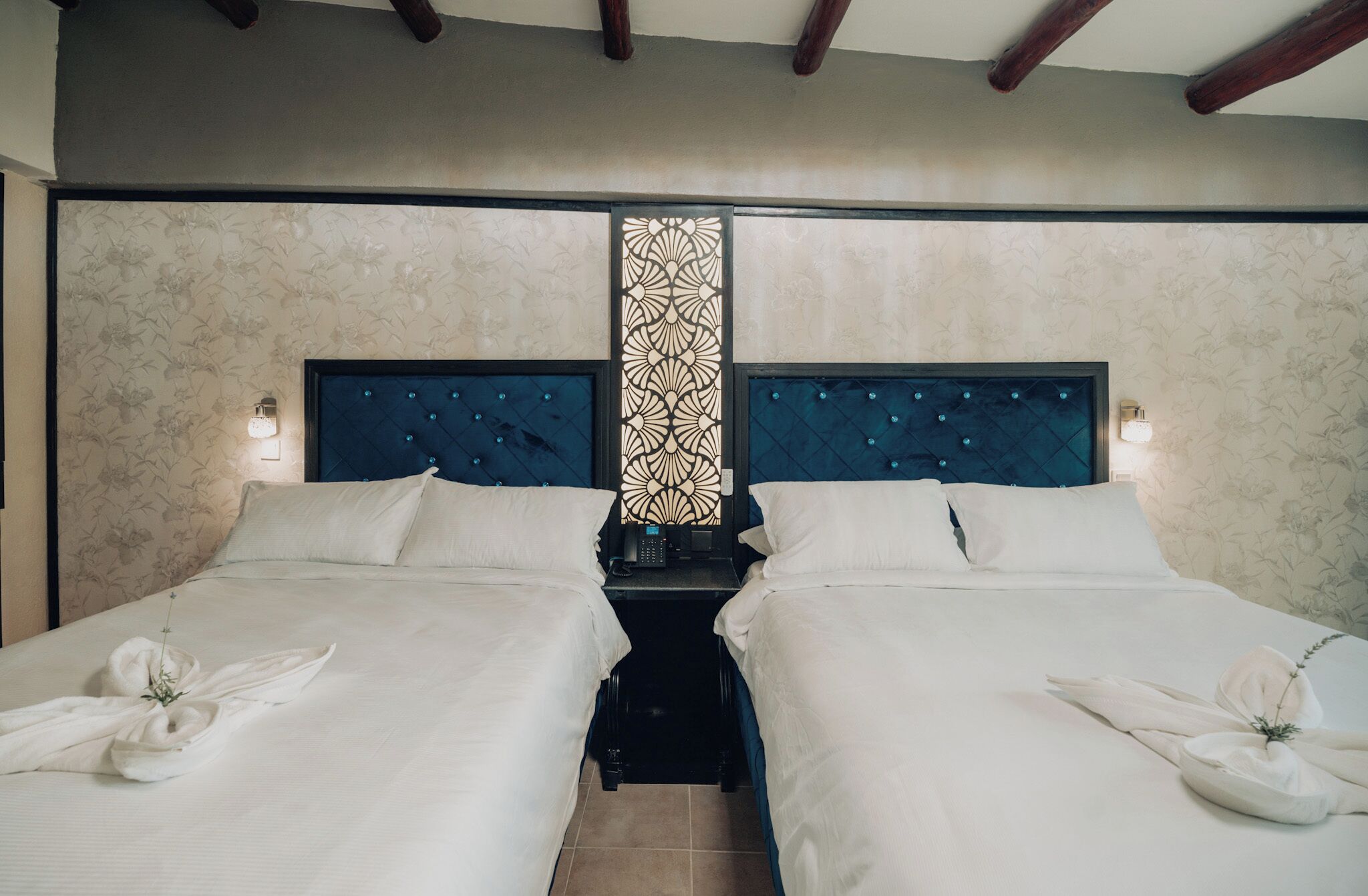 A double bed room with a dark blue headboard, a decorative vertical panel, and a small bedside table with a lamp.