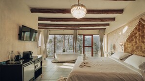 A bedroom with a large bed, a bathtub, and a TV on the wall.