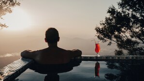 A person relaxing by a pool with a drink, surrounded by trees and a view of the water.