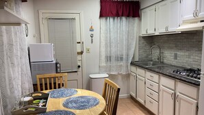 Una cocina con armarios blancos, encimera negra y salpicadero de azulejos. Hay una mesa de comedor con manteles individuales azules y sillas.