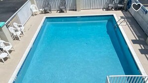 Una piscina rectangular con agua cristalina azul, rodeada por una solana blanca y una valla.