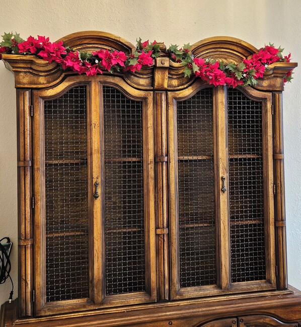 A wooden cabinet with a decorative top and a grid-patterned glass door.