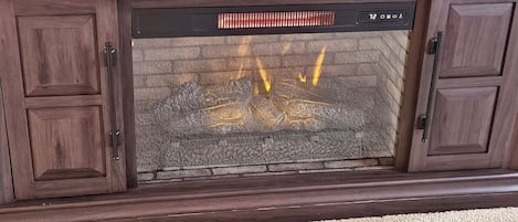 Una chimenea con revestimiento de piedra, una repisa de madera y un televisor montado encima.