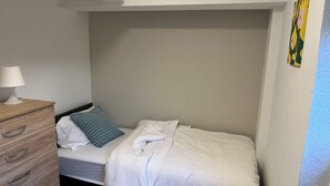 A small, single-bed room with a wooden dresser, a blue patterned pillow, and a white blanket. - 5 Bedroom Cosy Bloxwich Stay - Wifi & Free Parking (Walsall)