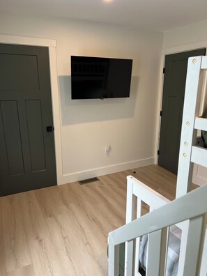 Una habitación con una televisión de pantalla plana en la pared, una escalera blanca y piso de madera.