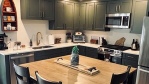 A modern kitchen with dark green cabinets, a wooden dining table, and four chairs. - The Maine Event- Wedding Weekend & Ski Getaways!  (Fryeburg)