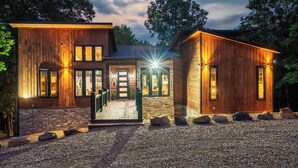 Une maison moderne en bois, dotée de fondations en pierre, de grandes fenêtres et d’une allée gravillonnée.