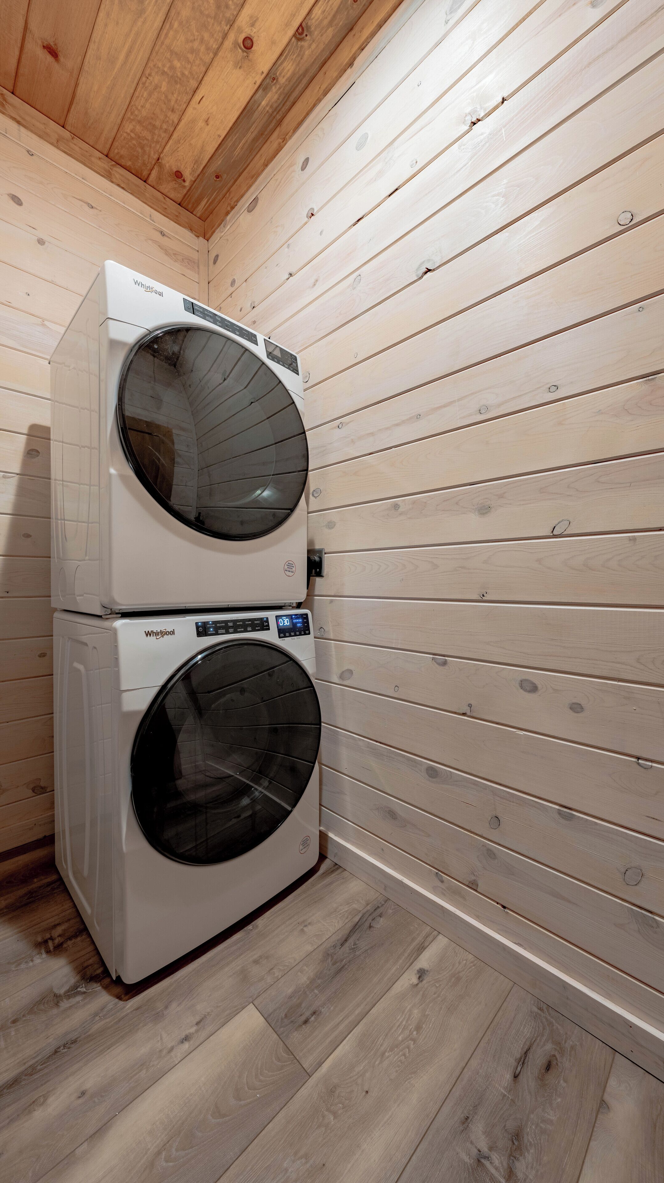 Eine Wasch- und Trockner-Kombination von Whirlpool mit zwei Türen in einem Raum mit Holzwandverkleidung und Holzboden.