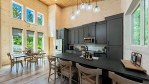 Une cuisine moderne avec des meubles de couleur sombre, un îlot central et un coin repas doté de chaises en bois.