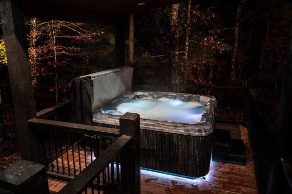 A hot tub in a forested area with a wooden deck and railings.