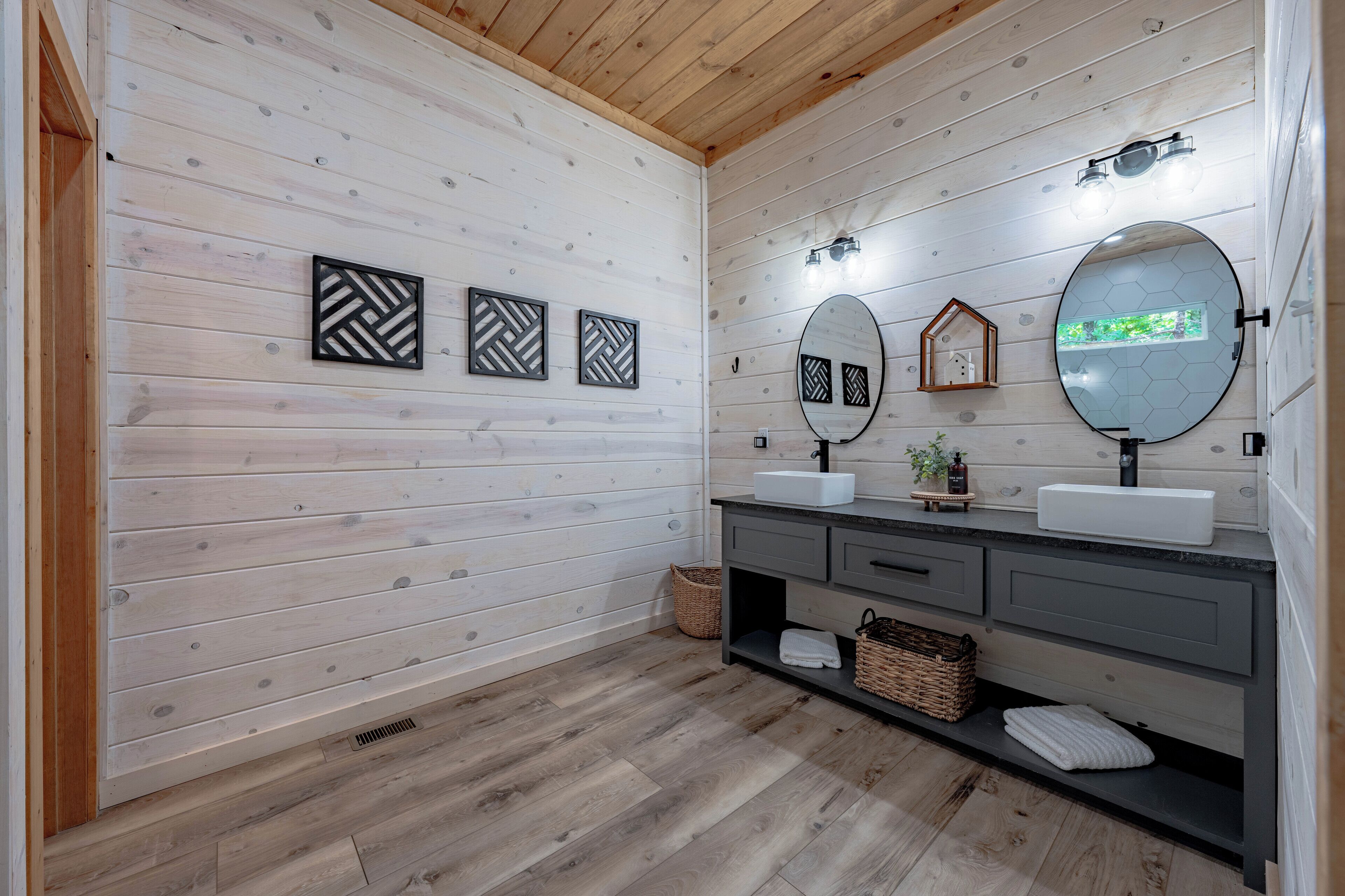 A bathroom with wooden walls, a wooden floor, a vanity with two sinks, and three wall-mounted mirrors.