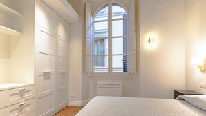 Ein Schlafzimmer mit einem großen Bett, einem Kleiderschrank, einem Fenster mit Rollläden und einer Wandleuchte.