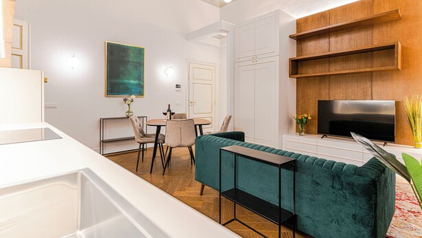 Ein modernes Wohnzimmer mit einem türkisfarbenen Sofa, einem Fernseher und einem Essbereich mit Stühlen und einem Tisch.