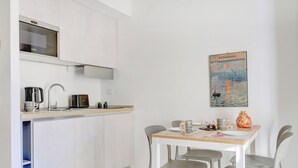 A modern kitchen with a built-in microwave, kettle, and coffee maker. There is a dining table with chairs and a poster on the wall. - Vatican Loft with Balcony -Home and More (Rome)