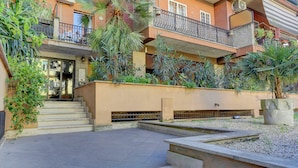 A multi-story residential building with balconies, air conditioning units, and a small courtyard with steps leading to the entrance. - Vatican Loft with Balcony -Home and More (Rome)