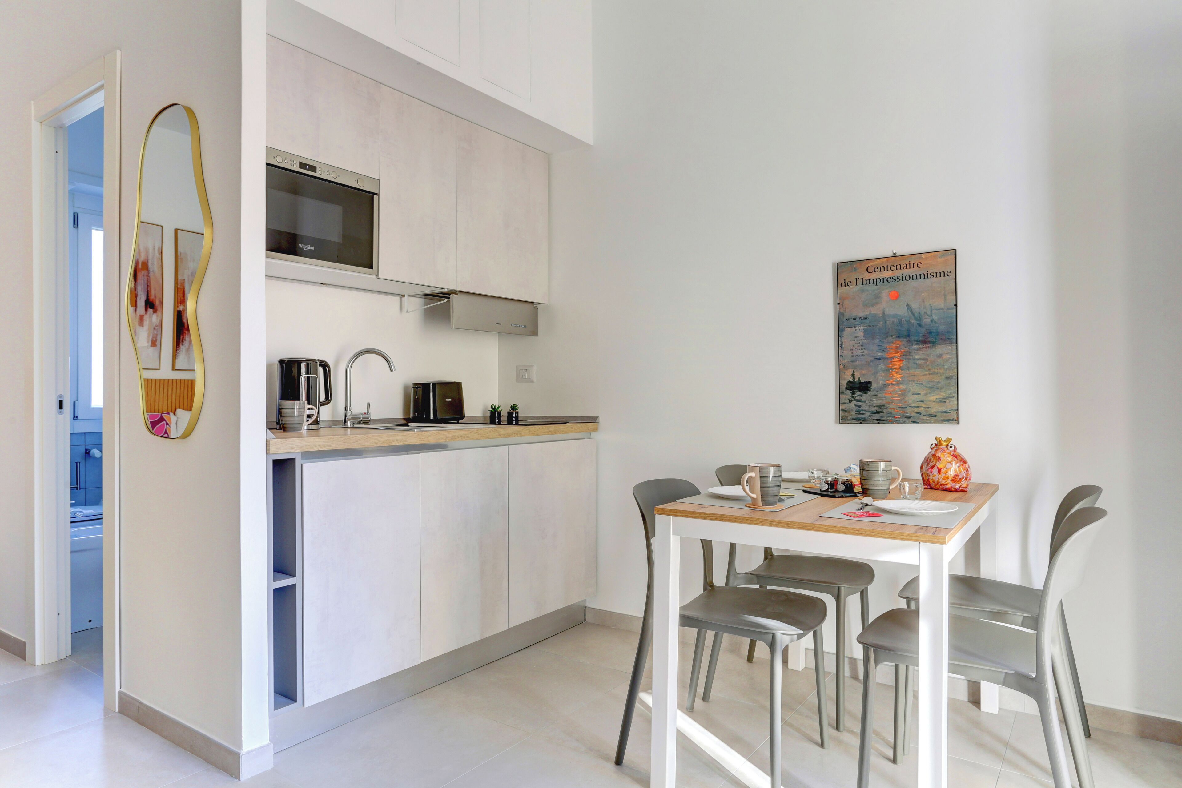A modern kitchen with a microwave, stove, and sink. There is a dining table with chairs and a painting on the wall.