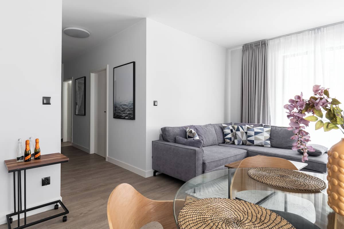 A modern living room with a grey sofa, a glass coffee table, and a wooden side table with bottles.