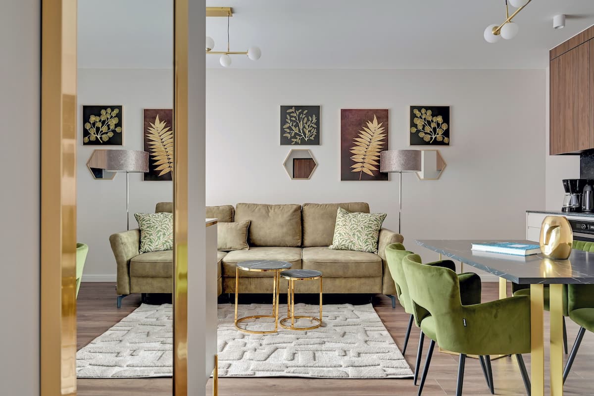 A modern living room with a sofa, two round tables, green chairs, and decorative wall art.