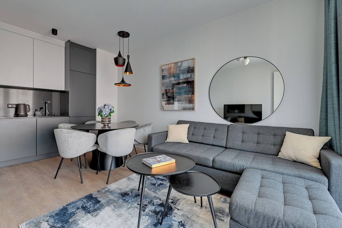 A modern living room with a grey sectional sofa, a round coffee table, and a dining area with a white table and chairs.
