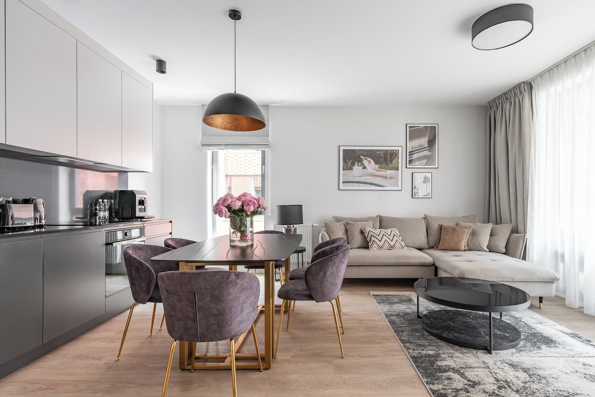 A modern living room with a sofa, a dining table with chairs, and a kitchen area with cabinets and appliances.