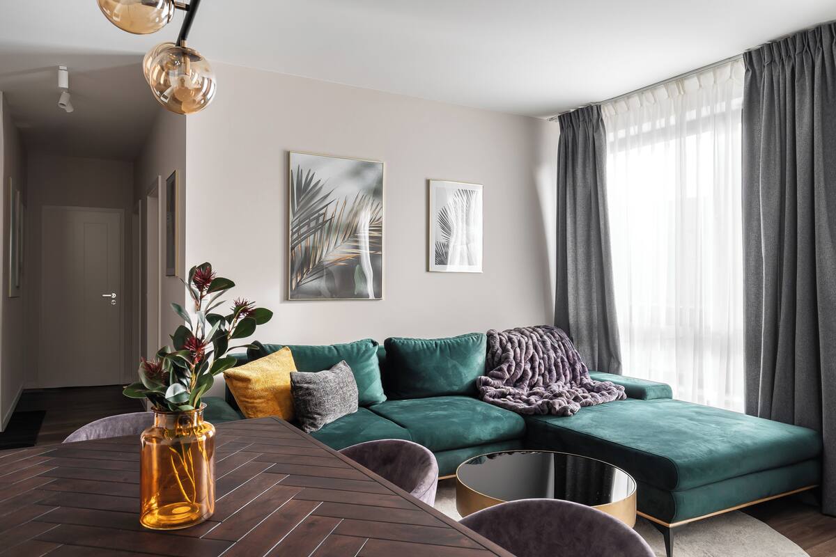 A modern living room with a green sofa, a coffee table, and a vase with flowers.